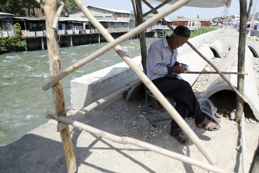 Мужчина пересчитывает кыргызские сомы, сидя в тенечке у реки Ак-Буура, протекающей через рынок.