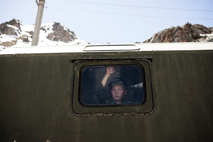 Кыргызский мальчишка смотрит из семейного вагончика на направляющихся в Россию трудовых мигрантов.